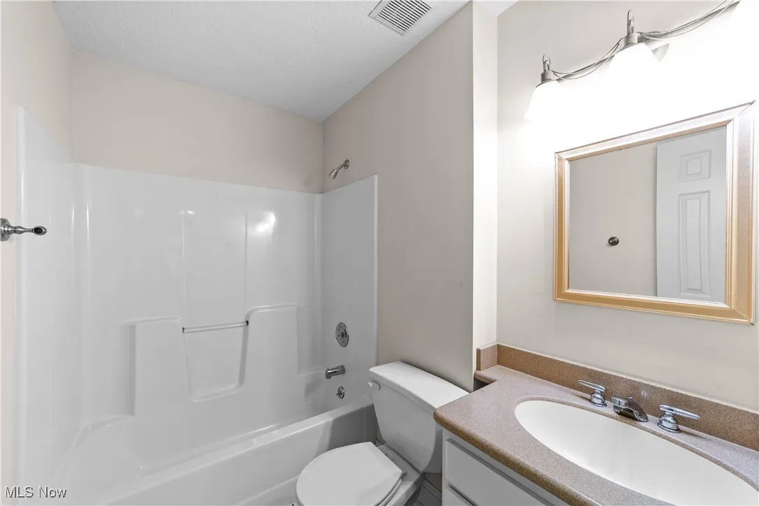 Full bath featuring washtub / shower combination, vanity, and a textured ceiling