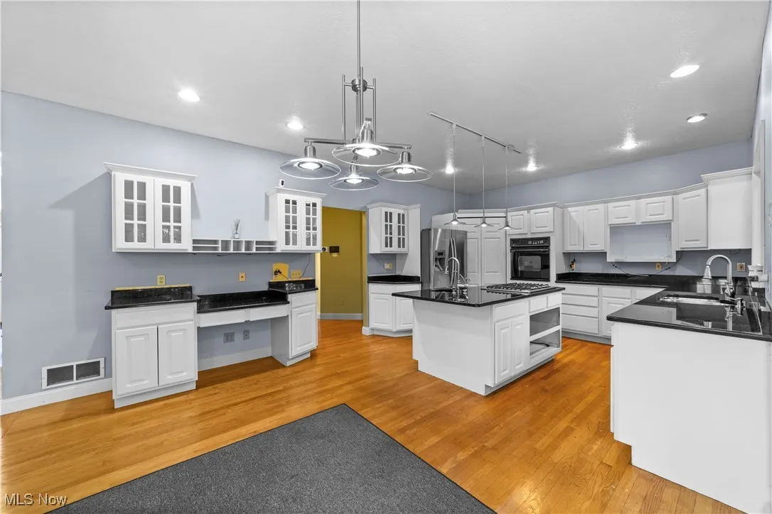 Kitchen featuring open shelves, a center island with sink, glass insert cabinets, light wood-type flooring, and recessed lighting