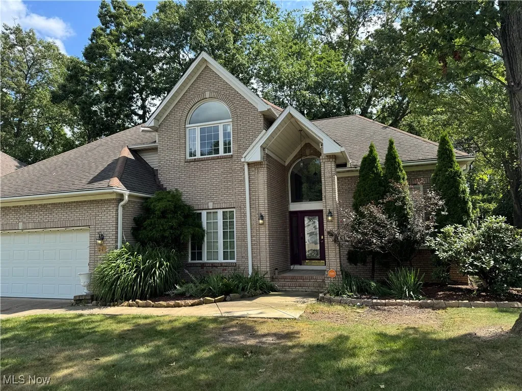 Traditional-style home featuring brick siding, a shingled roof, a garage, and a front lawn