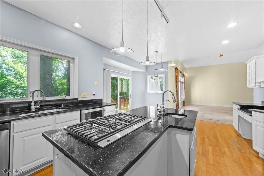 Kitchen featuring dark stone countertops, light wood finished floors, a center island with sink, white cabinets, and appliances with stainless steel finishes