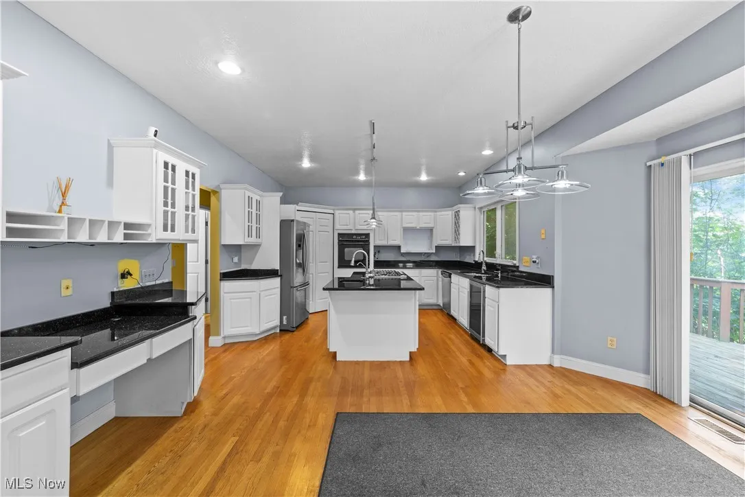 Kitchen with a center island with sink, glass insert cabinets, hanging light fixtures, open shelves, and light wood-style floors