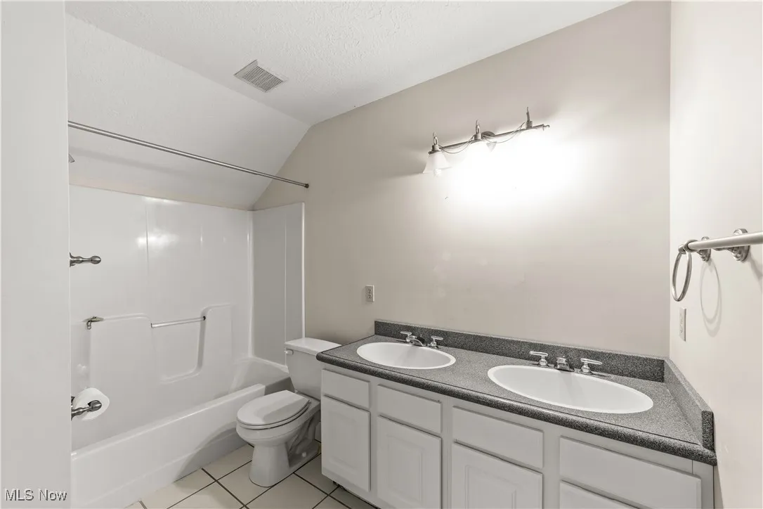 Bathroom with light tile patterned floors, double vanity, shower / tub combination, lofted ceiling, and a textured ceiling