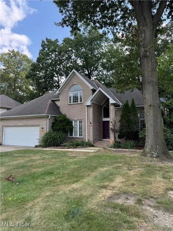 View of front facade with an attached garage, brick siding, a front lawn, driveway, and roof with shingles