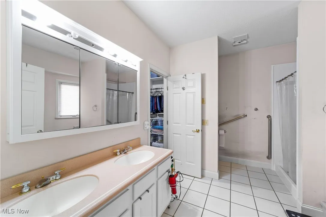 Bathroom featuring light tile patterned flooring, double vanity, a shower stall, and a walk in closet