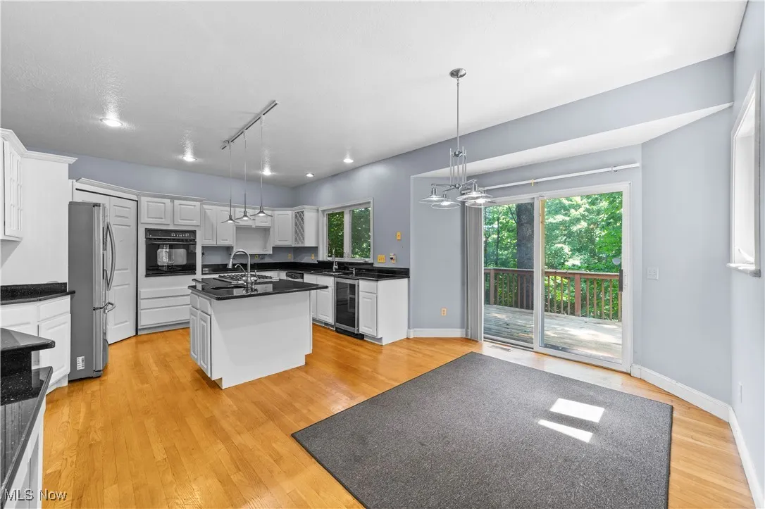 Kitchen featuring an island with sink, hanging light fixtures, a chandelier, black oven, and white cabinetry