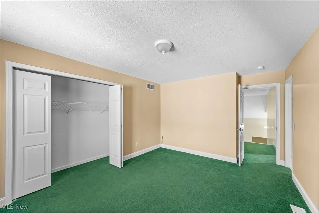 Unfurnished bedroom featuring a textured ceiling, dark carpet, and a closet