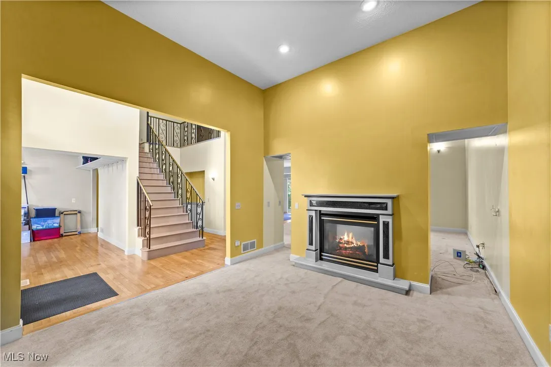 Unfurnished living room featuring a glass covered fireplace, carpet flooring, stairway, a towering ceiling, and recessed lighting