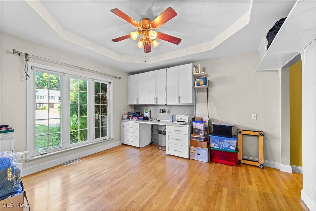Office space with a tray ceiling, light wood-type flooring, and a ceiling fan