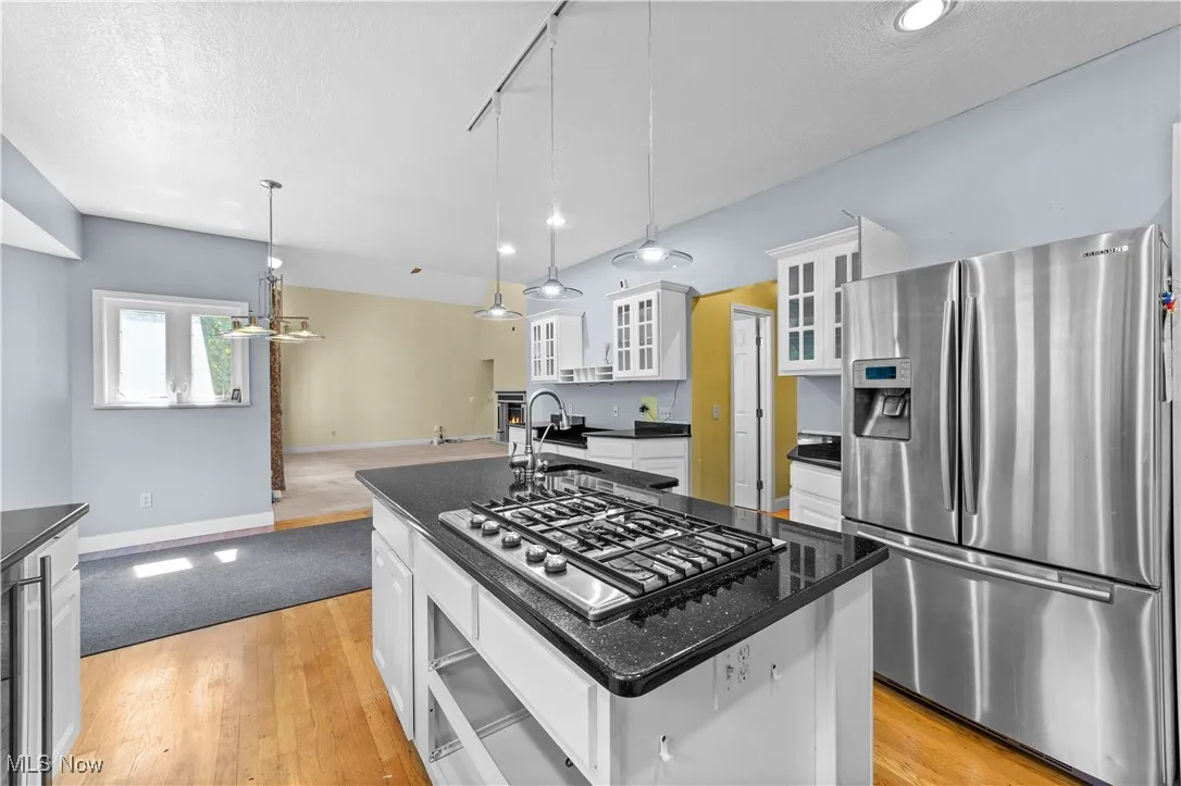 Kitchen with glass insert cabinets, appliances with stainless steel finishes, rail lighting, white cabinetry, and a kitchen island with sink