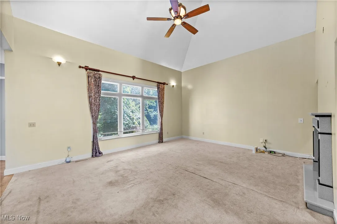 Unfurnished living room featuring light carpet, ceiling fan, and high vaulted ceiling