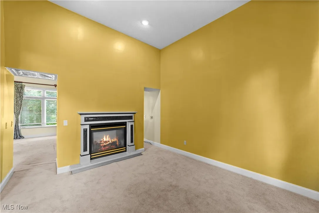 Unfurnished living room with a towering ceiling, a glass covered fireplace, and carpet flooring