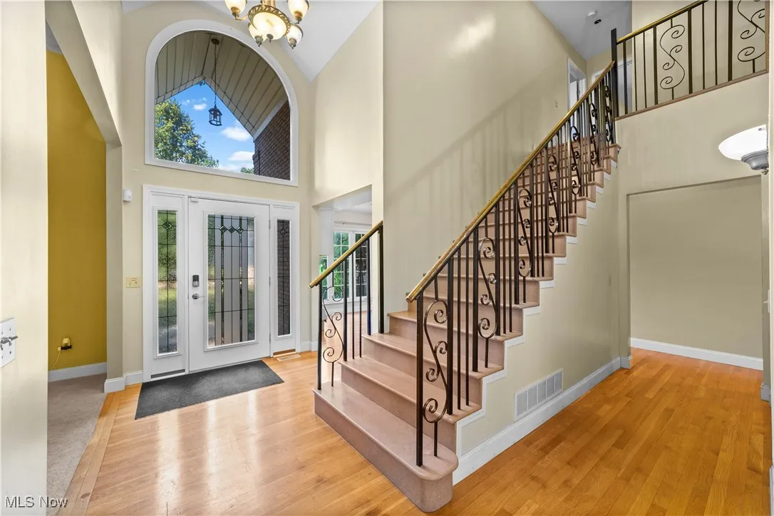 Foyer entrance featuring high vaulted ceiling, light wood-style flooring, a chandelier, and stairs