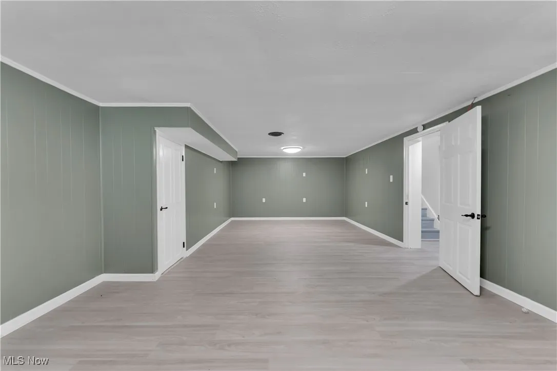 Unfurnished room with light wood-style flooring, crown molding, stairway, and wooden walls