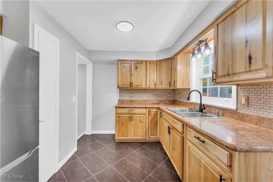 Kitchen featuring freestanding refrigerator, tasteful backsplash, light countertops, dark tile patterned flooring, and light brown cabinetry