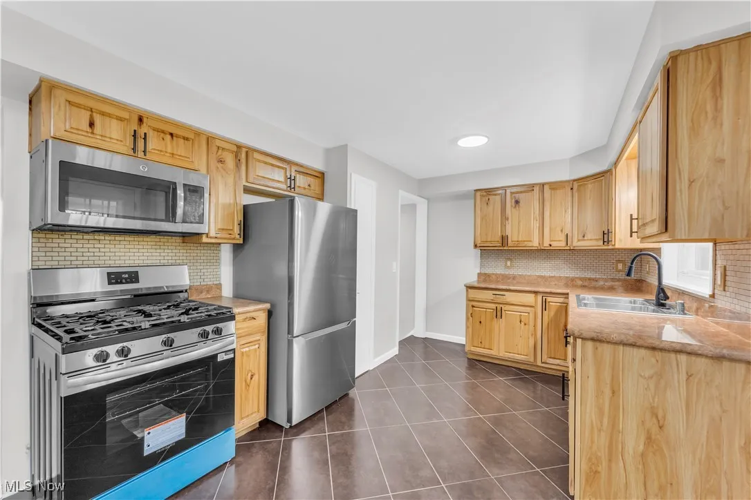 Kitchen with backsplash, appliances with stainless steel finishes, light countertops, dark tile patterned floors, and light brown cabinetry