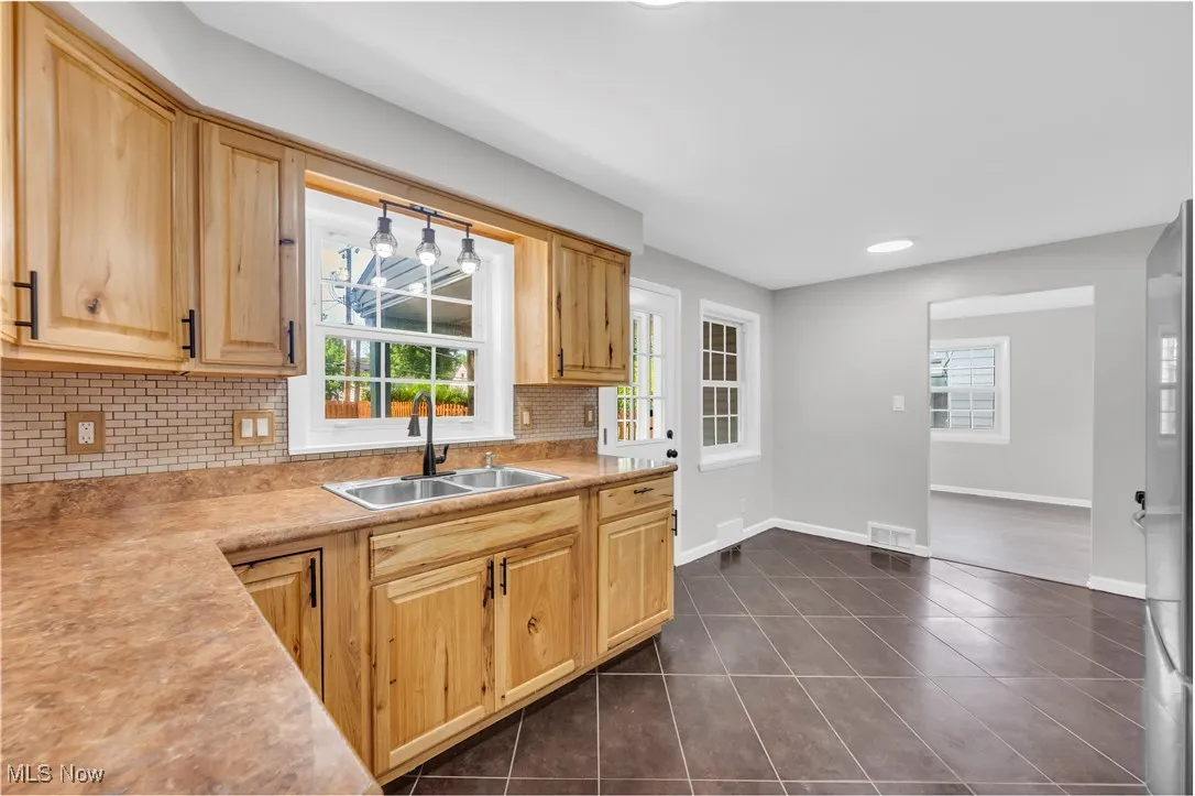 Kitchen featuring dark tile patterned floors, tasteful backsplash, light brown cabinetry, light countertops, and stainless steel fridge
