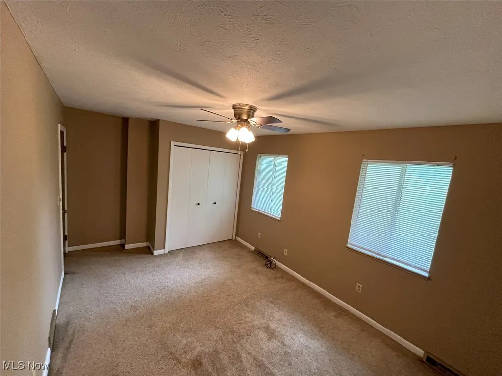 Carpeted empty room featuring a ceiling fan and baseboardscarpet, a textured ceiling, a closet, and a ceiling fan