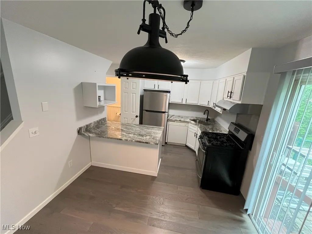 Kitchen view of newer white cabinets, granite counters including granite island, new light fixtures, stainless steel refrigerator/stove, dishwasher, and new lvt flooring.