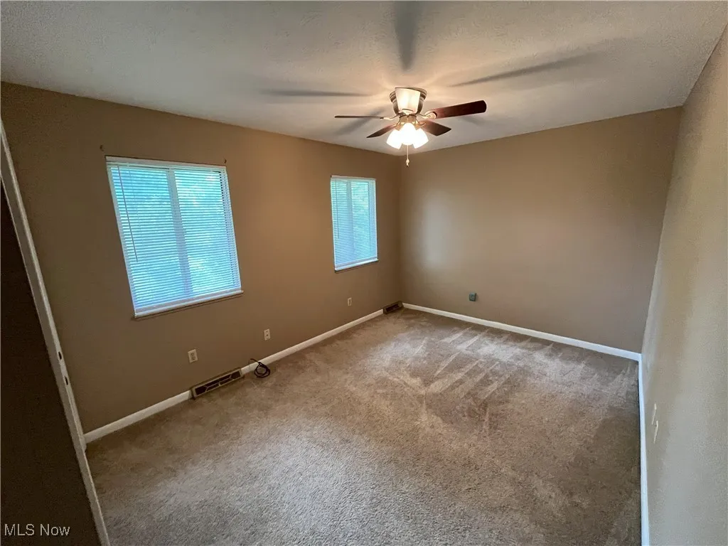 Carpeted empty room featuring a ceiling fan and baseboards