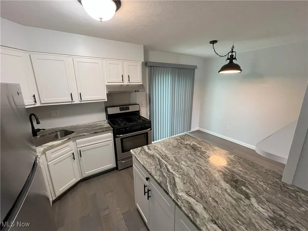 Kitchen view of newer white cabinets, granite counters including granite island, new light fixtures, stainless steel refrigerator/stove, dishwasher, and new lvt flooring.