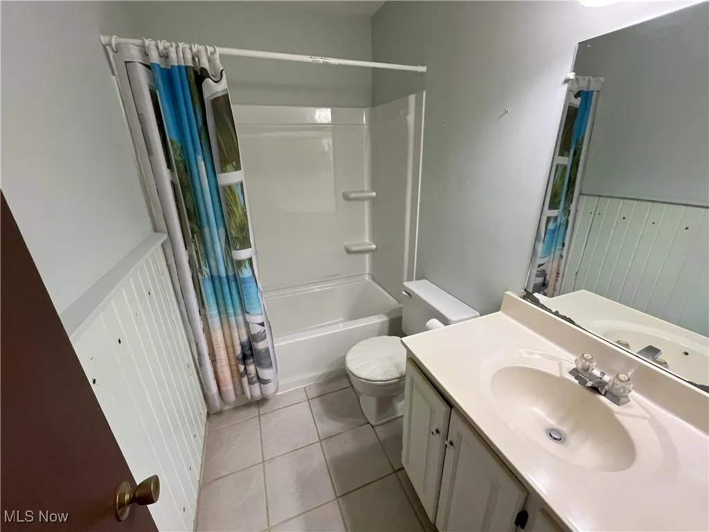Bathroom with new shower/bath, vanity, light tile patterned flooring, and wainscoting.