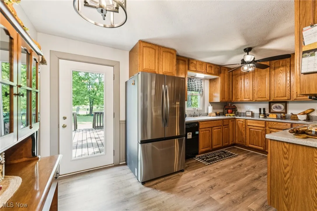 Kitchen featuring freestanding refrigerator, brown cabinets, light wood-type flooring, black dishwasher, and light countertops