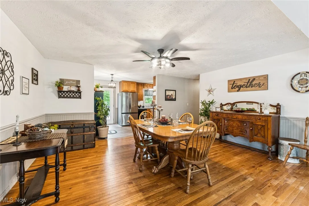 Dining space featuring wainscoting, light wood-style flooring, ceiling fan, and a textured ceiling