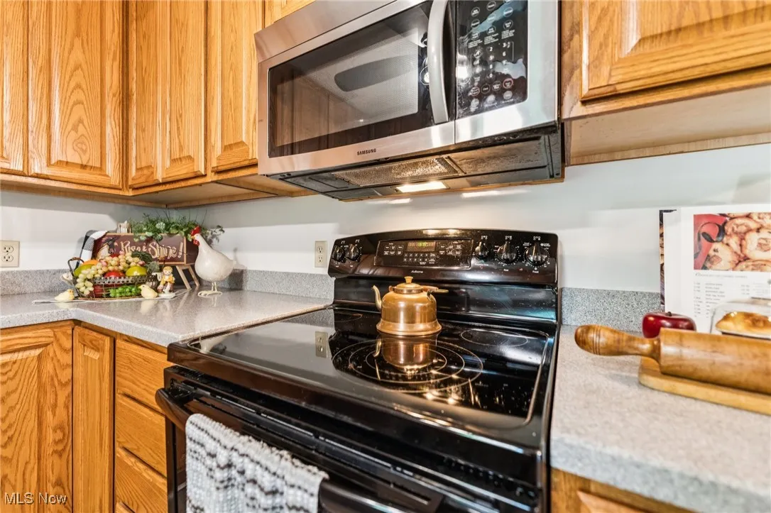Kitchen with black electric range oven, stainless steel microwave, and light countertops