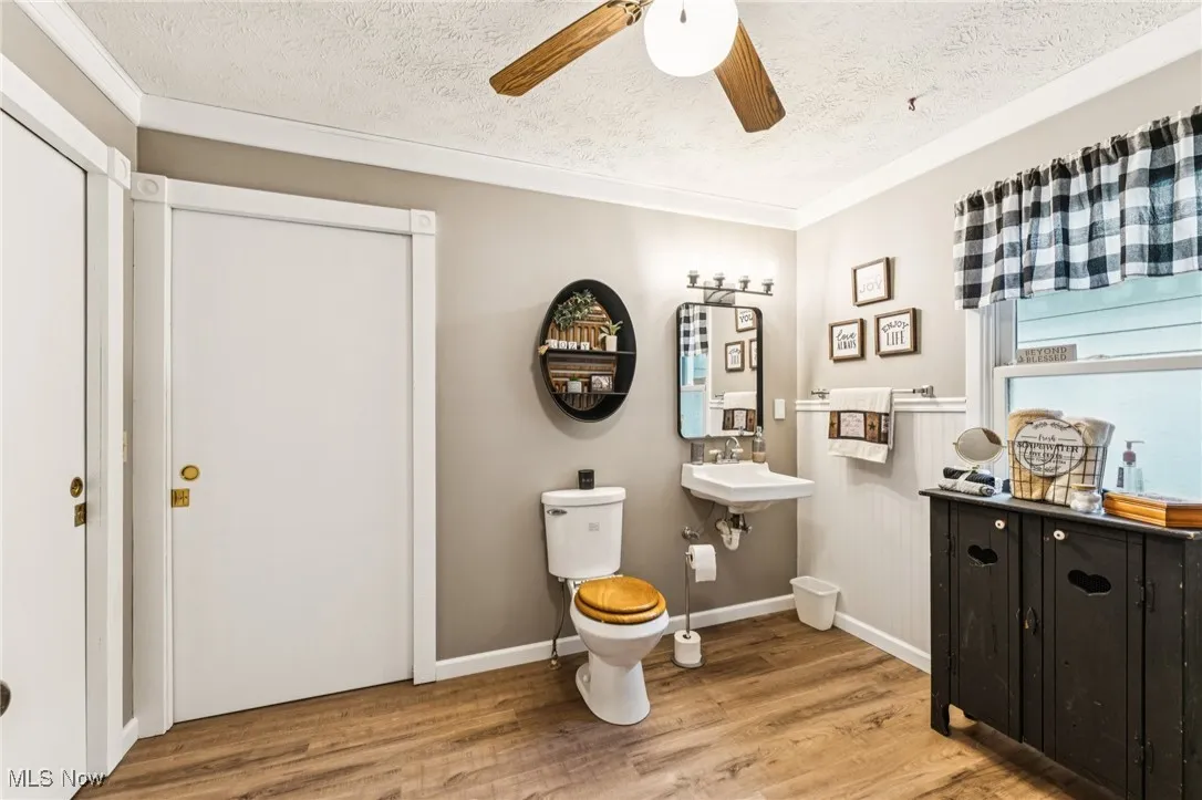 Bathroom with a textured ceiling, wood finished floors, ceiling fan, and crown molding