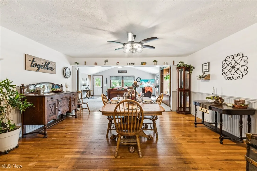 Dining area with wood-type flooring, a textured ceiling, ceiling fan, and vaulted ceiling
