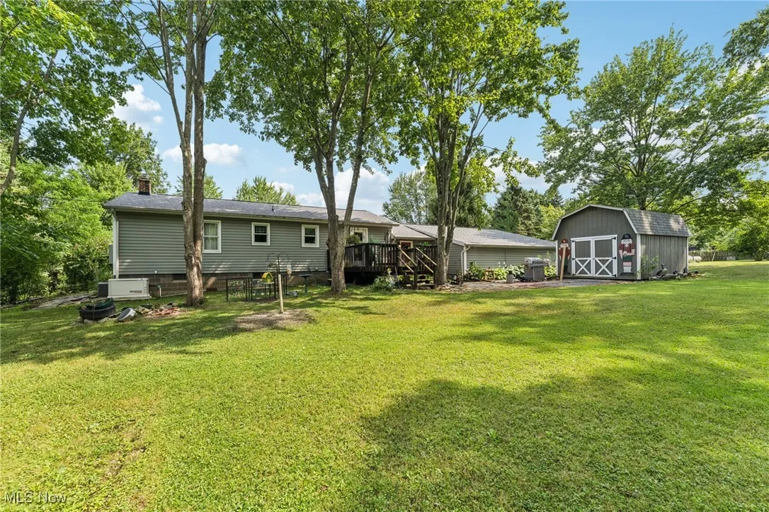 Rear view of property featuring a storage unit, a lawn, a deck, and a chimney