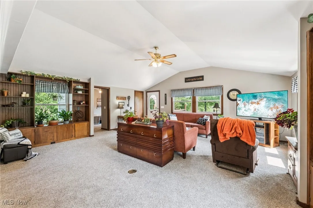 Carpeted living area featuring vaulted ceiling and ceiling fan