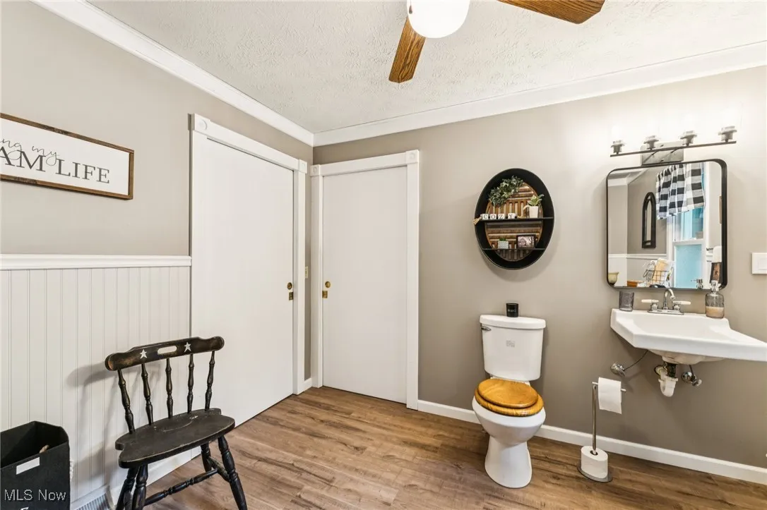 Half bath featuring a textured ceiling, wood finished floors, crown molding, and a ceiling fan