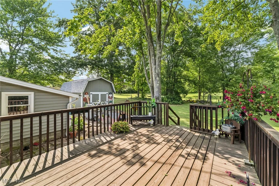 Wooden terrace featuring a storage shed, view of wooded area, and a lawn