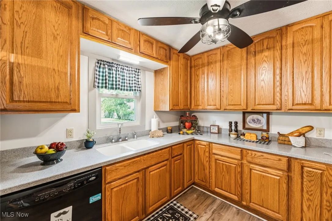 Kitchen featuring black dishwasher, wood finished floors, light countertops, brown cabinetry, and a ceiling fan