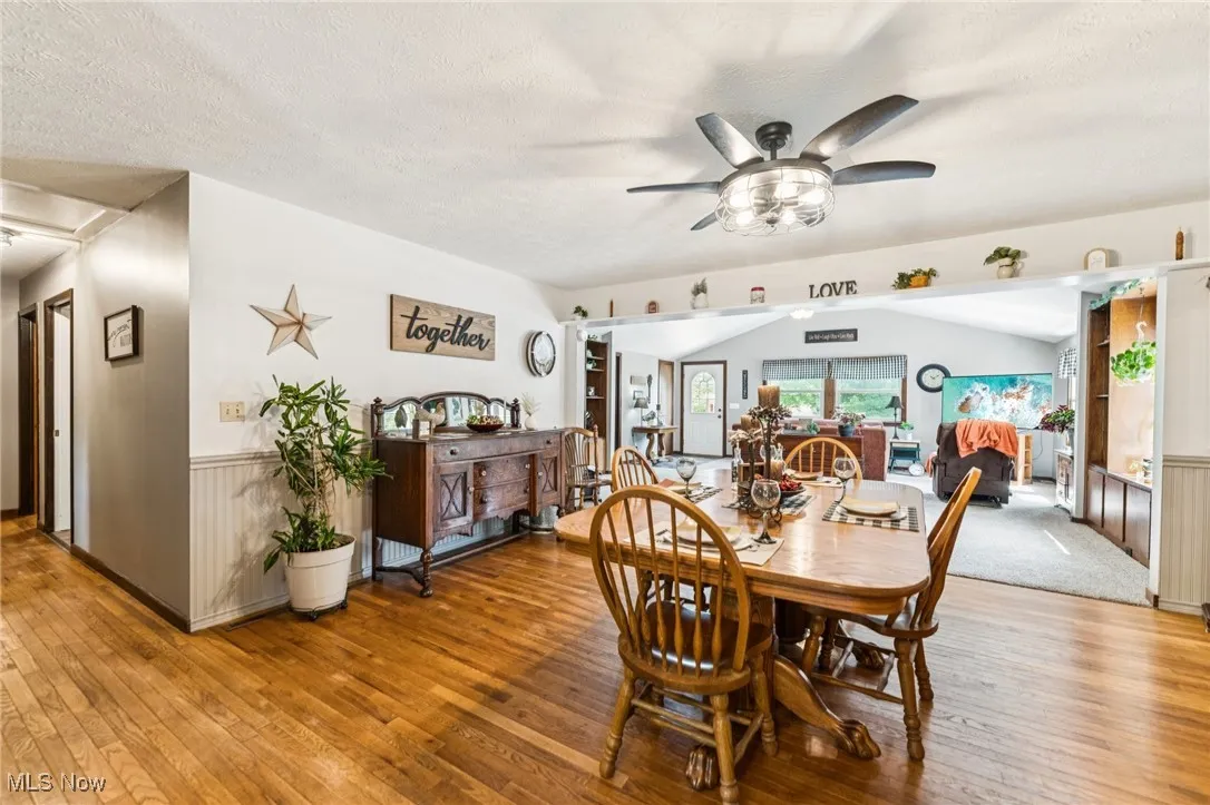 Dining space featuring a wainscoted wall, ceiling fan, hardwood / wood-style flooring, a textured ceiling, and vaulted ceiling