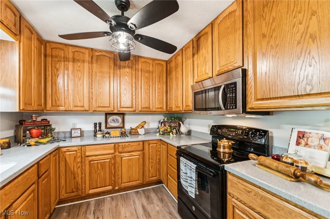 Kitchen with black range with electric stovetop, light wood-style flooring, light countertops, and brown cabinets