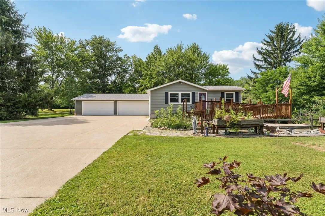 View of front of property featuring a garage, a wooden deck, a front lawn, concrete driveway, and view of wooded area