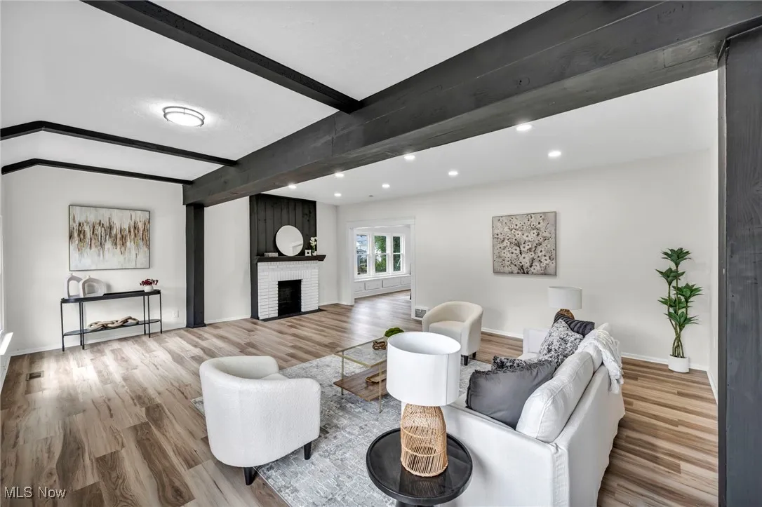 Living area with beamed ceiling, light wood-style floors, a brick fireplace, and recessed lighting