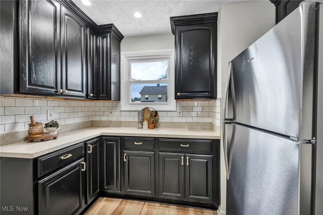 Kitchen featuring dark cabinets, freestanding refrigerator, a textured ceiling, light stone counters, and recessed lighting