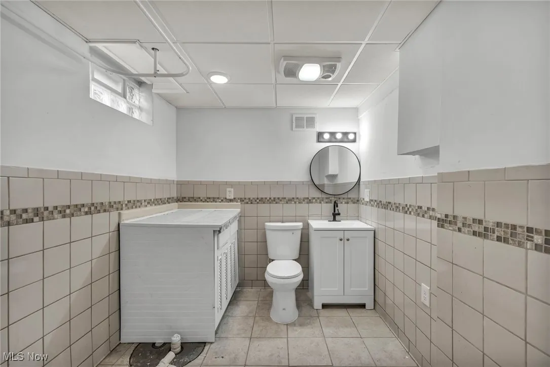 Bathroom featuring light tile patterned floors, vanity, tile walls, wainscoting, and recessed lighting