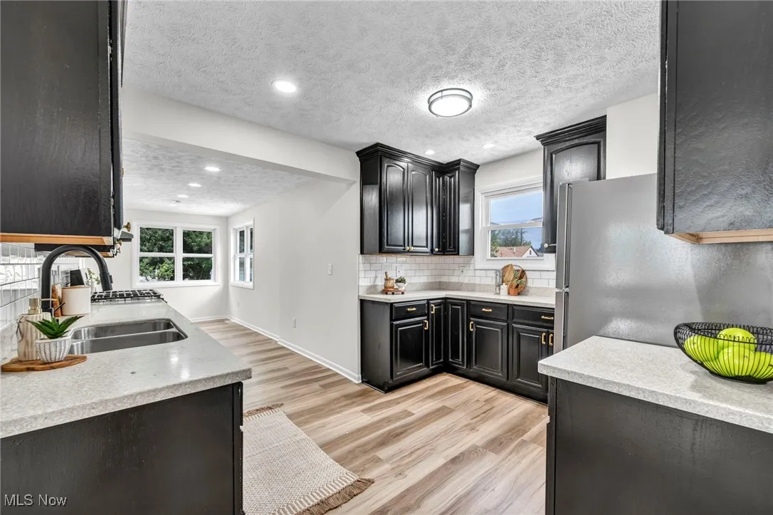 Kitchen with a textured ceiling, light wood-style floors, dark cabinetry, backsplash, and light stone countertops