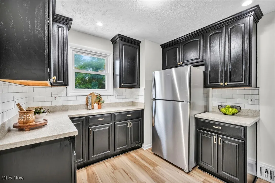 Kitchen featuring freestanding refrigerator, light wood-style flooring, light stone counters, dark cabinetry, and a textured ceiling