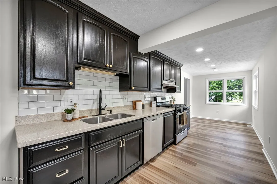 Kitchen featuring a textured ceiling, appliances with stainless steel finishes, decorative backsplash, dark cabinetry, and light stone countertops