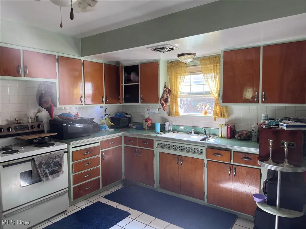 Kitchen featuring white range oven, tasteful backsplash, light tile patterned flooring, and light countertops