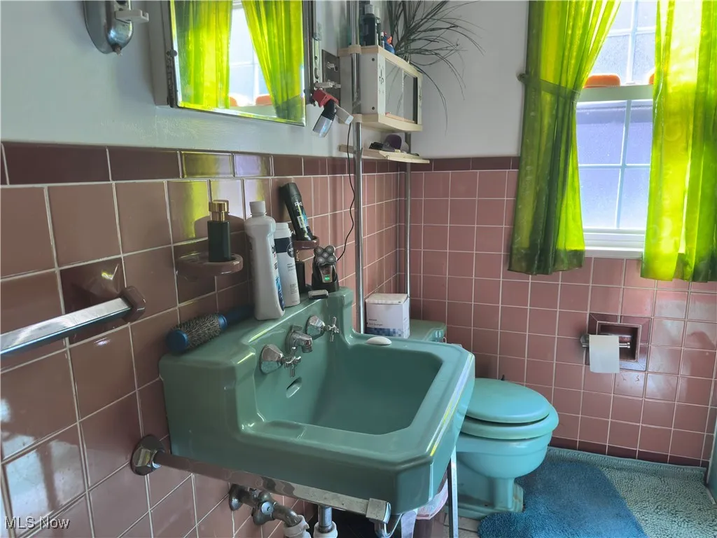 Half bathroom featuring healthy amount of natural light, tile walls, and wainscoting
