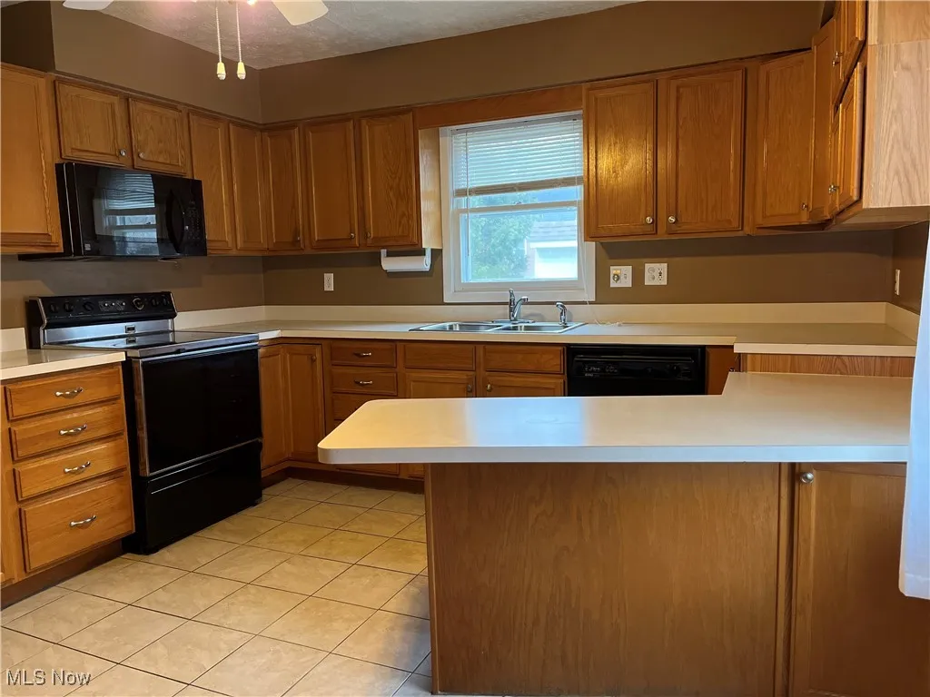 Kitchen featuring black appliances, light countertops, brown cabinetry, a peninsula, and light tile patterned floors