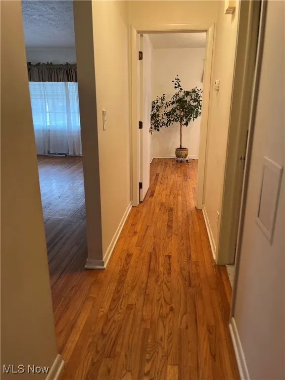 Corridor with light wood-type flooring and a textured ceiling