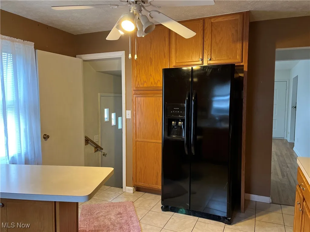 Kitchen featuring brown cabinets, black fridge, light tile patterned floors, light countertops, and a textured ceiling