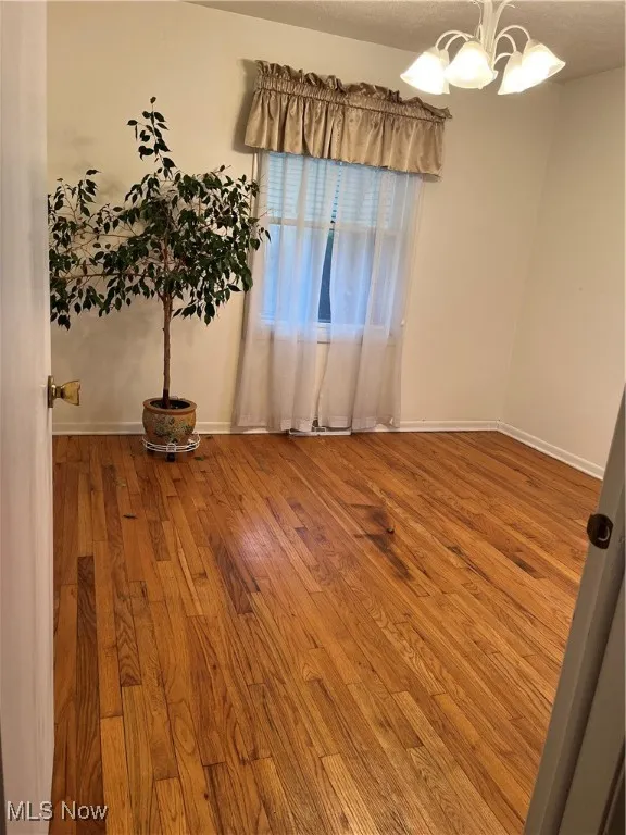 Empty room featuring hardwood / wood-style floors, a chandelier, and a textured ceiling
